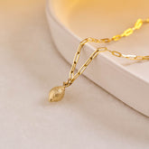 A yellow gold miniature lemon jewellery charm on a yellow gold paper clip chain.